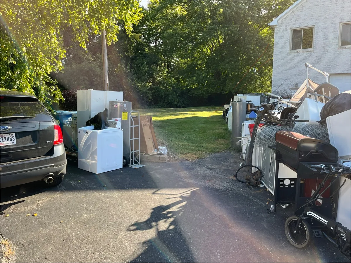 Water heaters, a washer, chain-link fencing, and mixed metal staged on an Indianapolis driveway ahead of a pickup