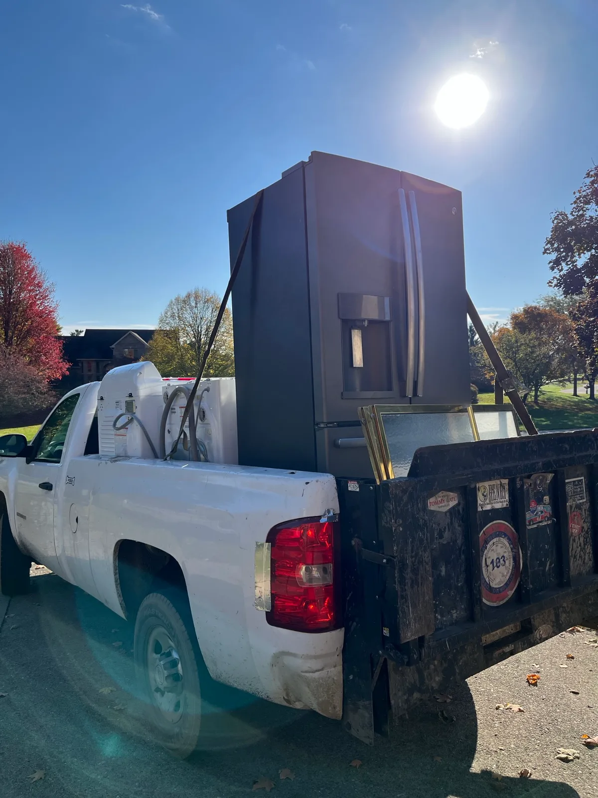 Side-by-side refrigerator and a framed window loaded on a dump bed during a fall curbside pickup in Indianapolis