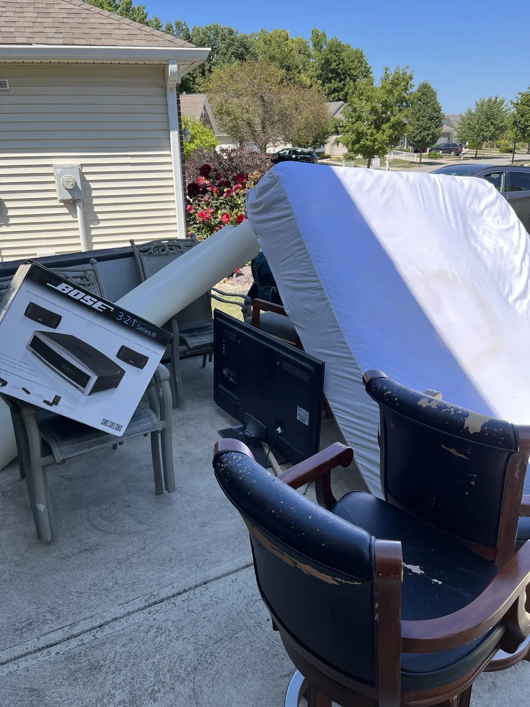 Two worn armchairs with peeling upholstery staged on an Indianapolis driveway beside a mattress and TV for pickup